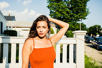 Young woman in orange top posing on sunny porch