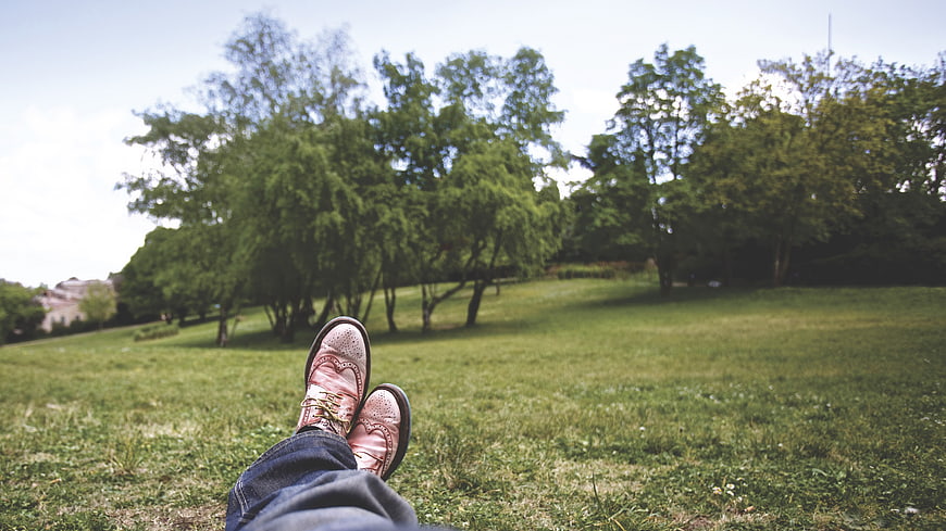 Relaxed man's feet in brown shoes on grassy park