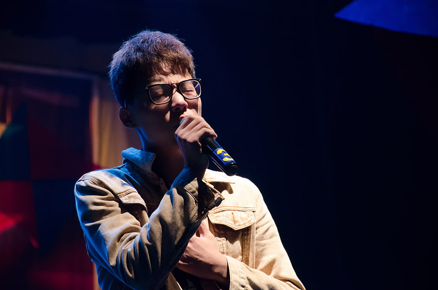 Young Asian man singing passionately into microphone on stage