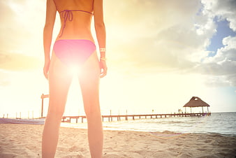 Woman in pink bikini standing on tropical beach at sunset