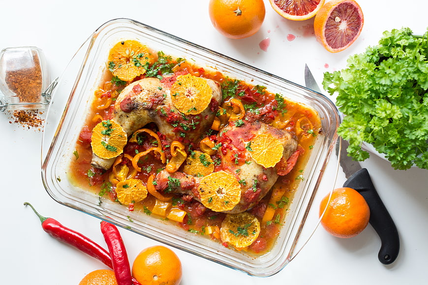 Roasted chicken legs with oranges and peppers in glass dish