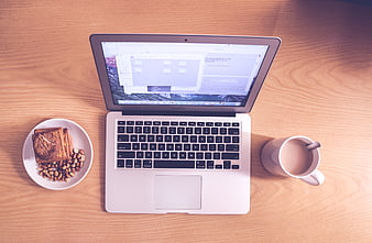 Flat lay of laptop, coffee, and breakfast on wooden desk