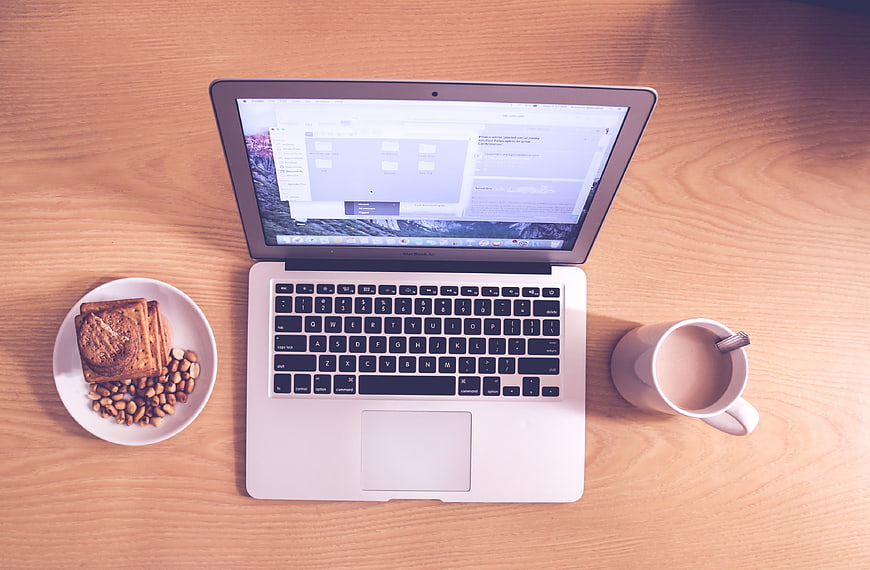 Flat lay of laptop, coffee, and breakfast on wooden desk