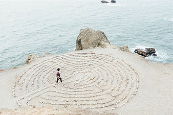 Woman walking on coastal stone labyrinth near ocean