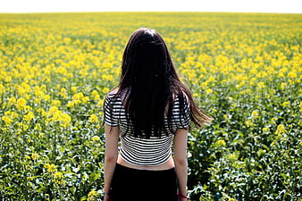 Woman with long dark hair standing in yellow rapeseed field