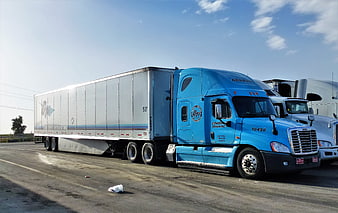 Blue semi-truck with white trailer parked in a logistics yard