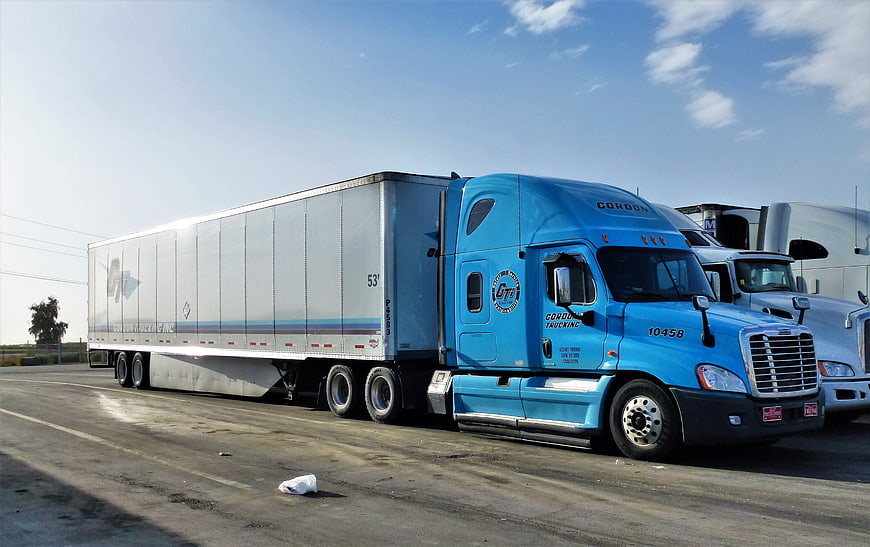Blue semi-truck with white trailer parked in a logistics yard