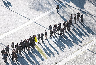 Aerial view of people queuing on cobblestone plaza with long shadows