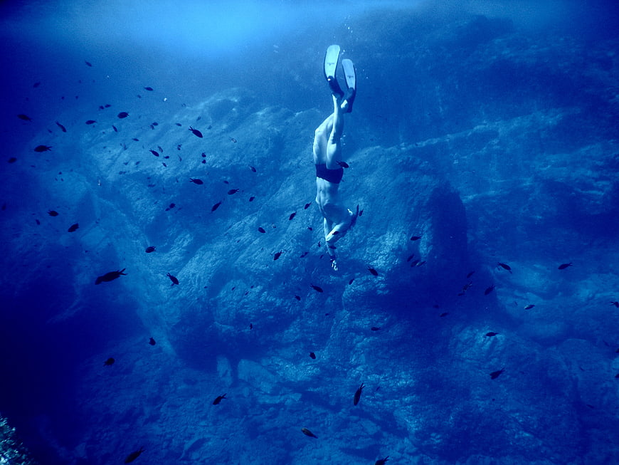Underwater diver swimming near rocky reef with fish