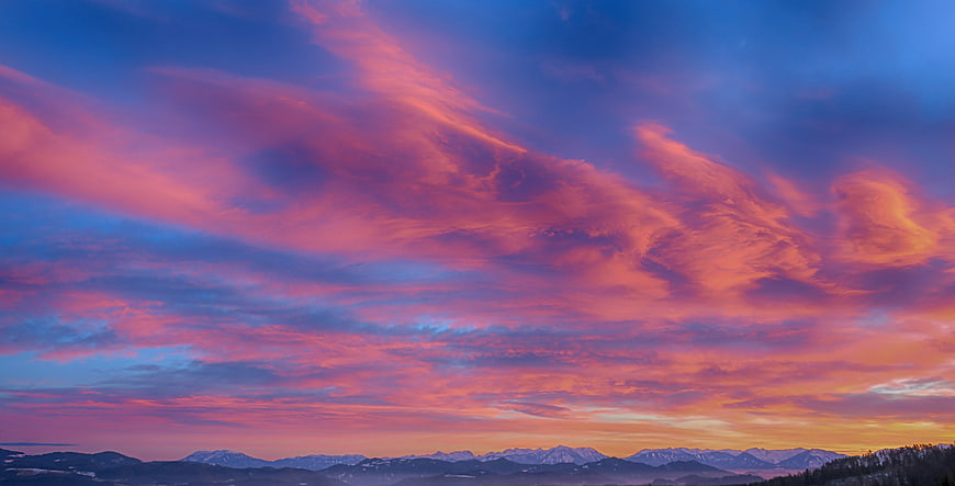 Vibrant pink and purple sunset clouds over snowy mountain range