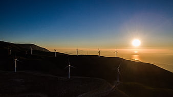 Wind turbines on rolling hills at sunset over ocean