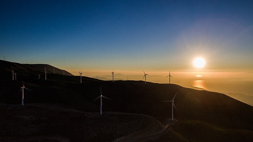 Wind turbines on rolling hills at sunset over ocean