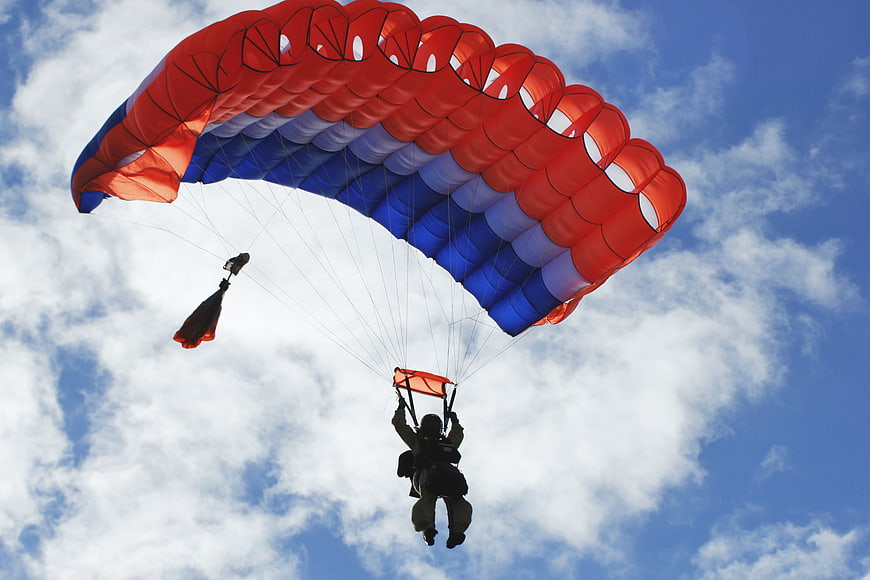 Paratrooper descending with red and blue parachute against blue sky