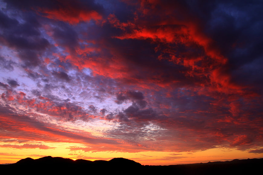 Dramatic red and purple sunset clouds over silhouetted mountains