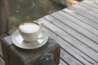 Cappuccino on rustic wooden post by water
