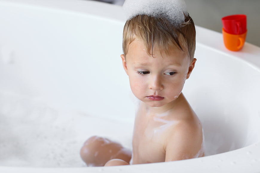 Toddler boy with soap bubbles in white bathtub