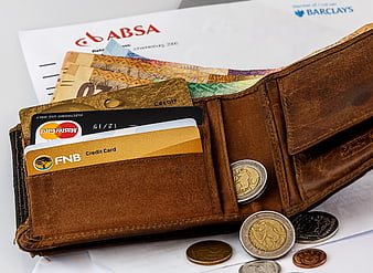 Open leather wallet with credit cards, cash, and coins on bank statements