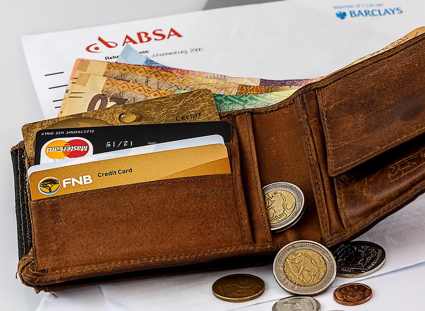 Open leather wallet with credit cards, cash, and coins on bank statements