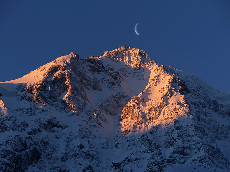 Crescent Moon over Snow-Capped Mountain Peak at Sunset