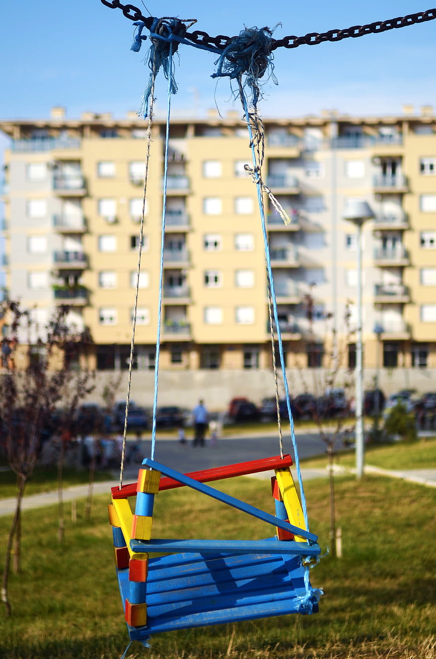 Colorful Wooden Swing in Urban Park with Apartment Background