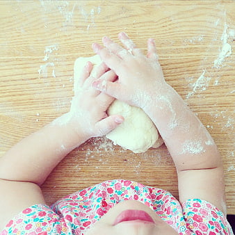 Child kneading dough on wooden table with flour