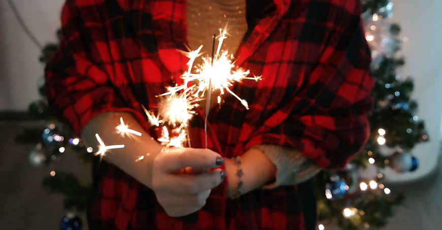 Person holding sparklers in red plaid shirt near Christmas tree