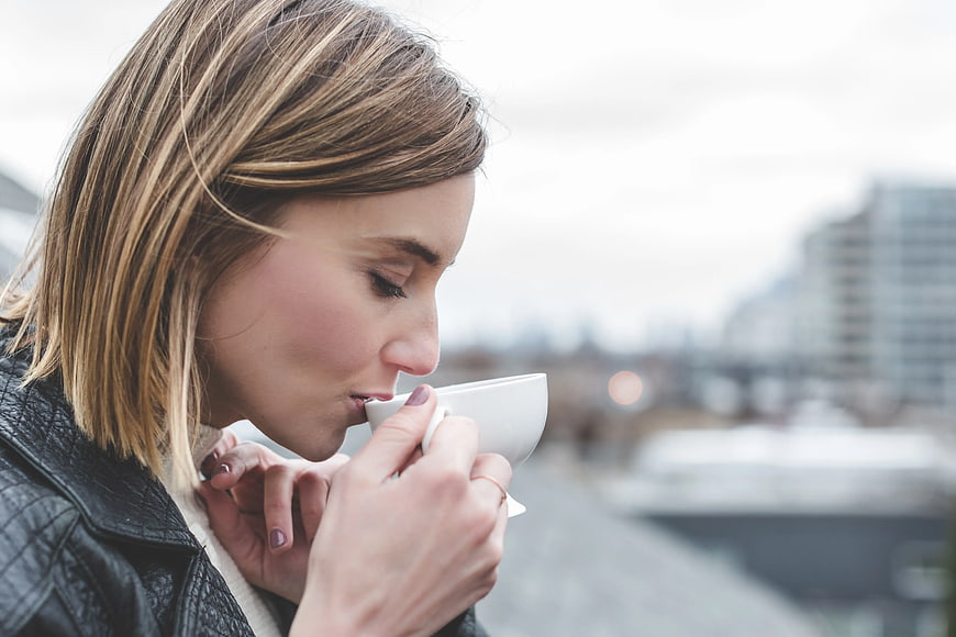 Woman Sipping Coffee from White Cup Outdoors
