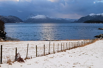 Snowy coastal landscape with wooden fence and fjord mountains