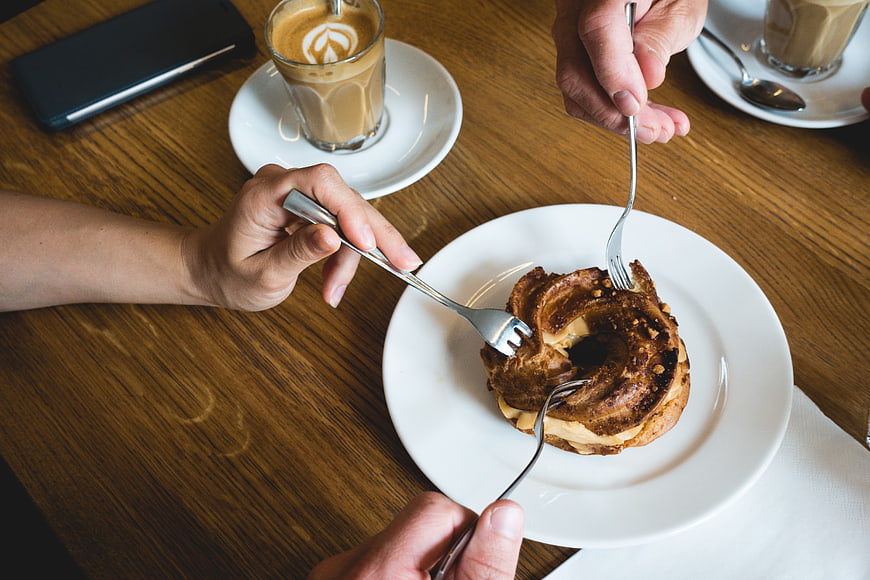 Hands Sharing Cinnamon Roll with Coffee on Wooden Table