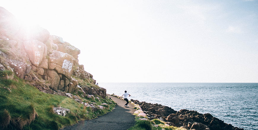 Skateboarder Riding Coastal Path Near Rocky Cliffs