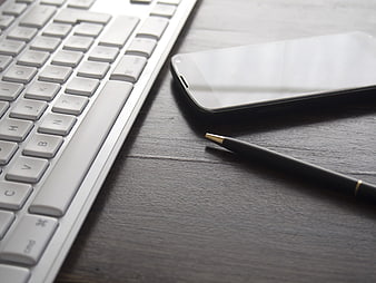 White keyboard, smartphone, and pen on dark wooden desk