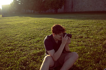 Young male photographer taking photo in grassy field at sunset