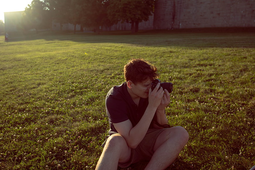 Young male photographer taking photo in grassy field at sunset