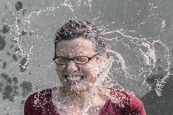 Woman with glasses grimacing as water splashes on her face