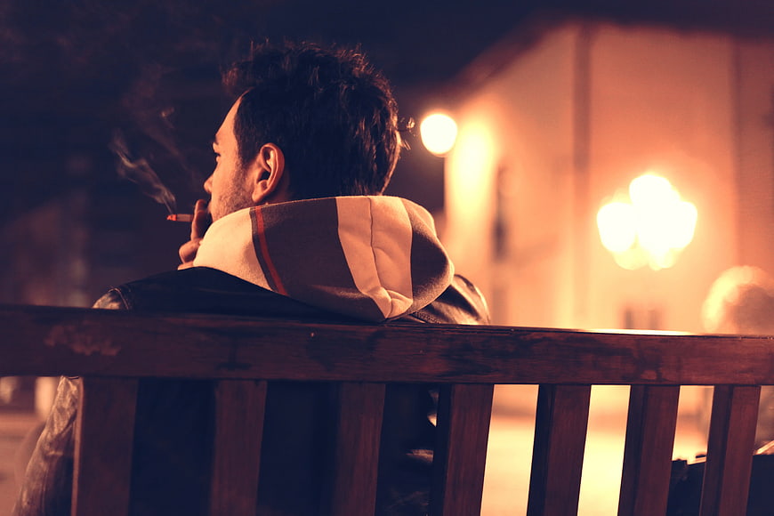 Man Smoking on Bench at Night with Bokeh Lights