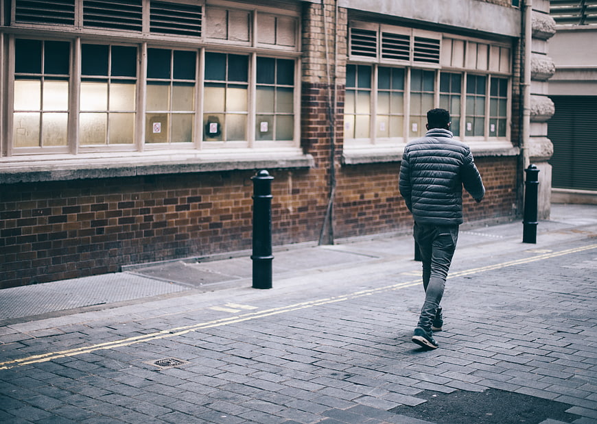Man in Puffer Jacket Walking Away on Cobblestone Street