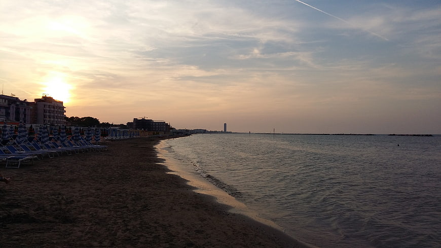 Sunset over a quiet beach with folded blue umbrellas and calm sea
