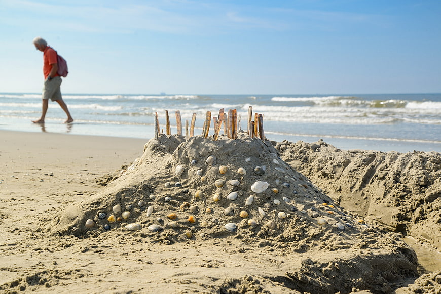 Sandcastle with shells on beach with man walking