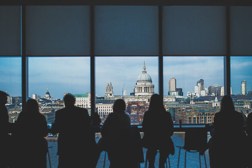 Silhouettes of people looking at London skyline from window