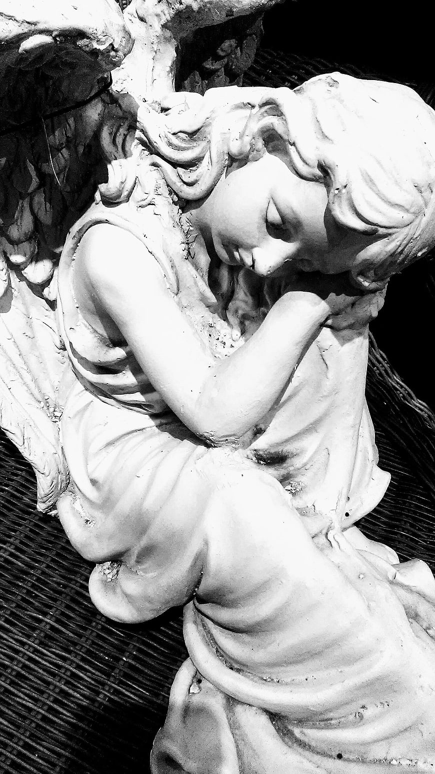 Black and white close-up of a weathered stone angel statue