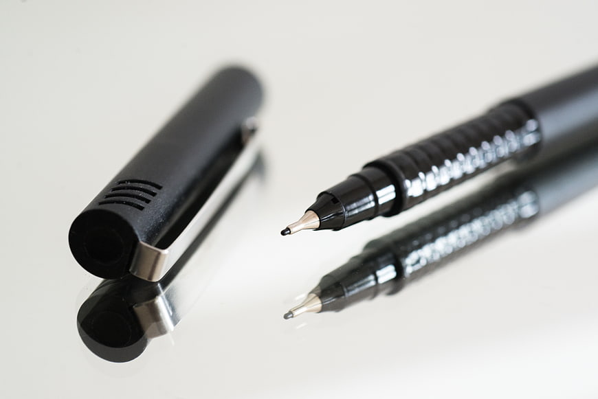 Close-up of black pen and cap on white reflective surface