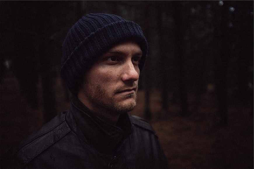 Pensive man in beanie and jacket in dark forest