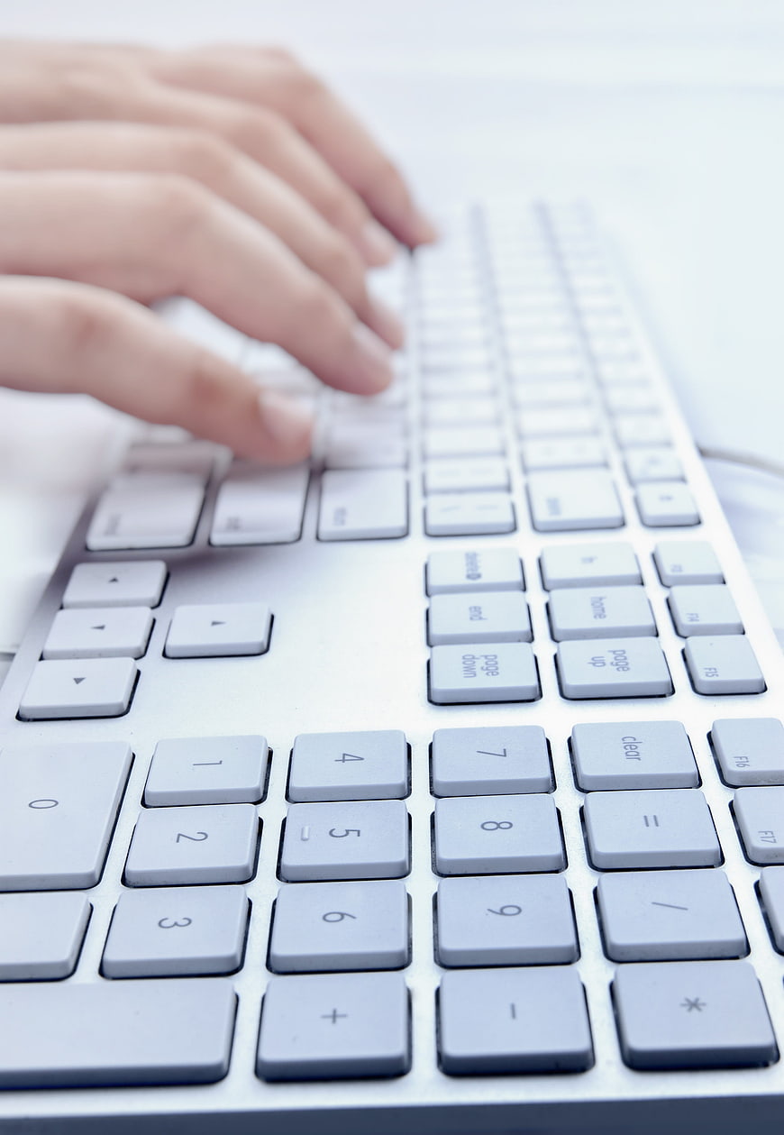 Close-up of hands typing on a white computer keyboard