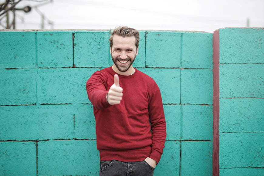 Happy Man Giving Thumbs Up Against Teal Brick Wall