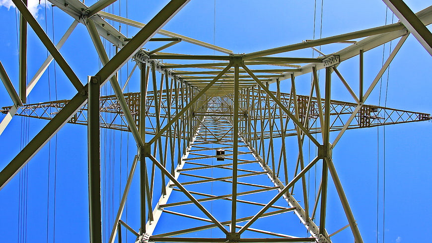 Low angle view of steel electricity pylon against blue sky