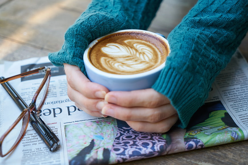 Hands holding cappuccino with latte art on newspaper