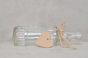 Empty glass bottle with heart tag and twine on white background