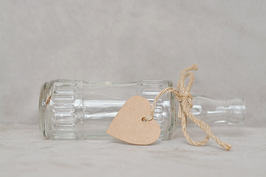 Empty glass bottle with heart tag and twine on white background