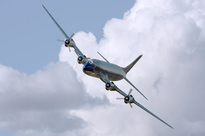 Vintage Chrome Propeller Airplane Flying in Cloudy Sky