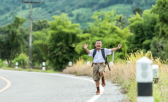 Happy schoolboy running on rural road with backpack